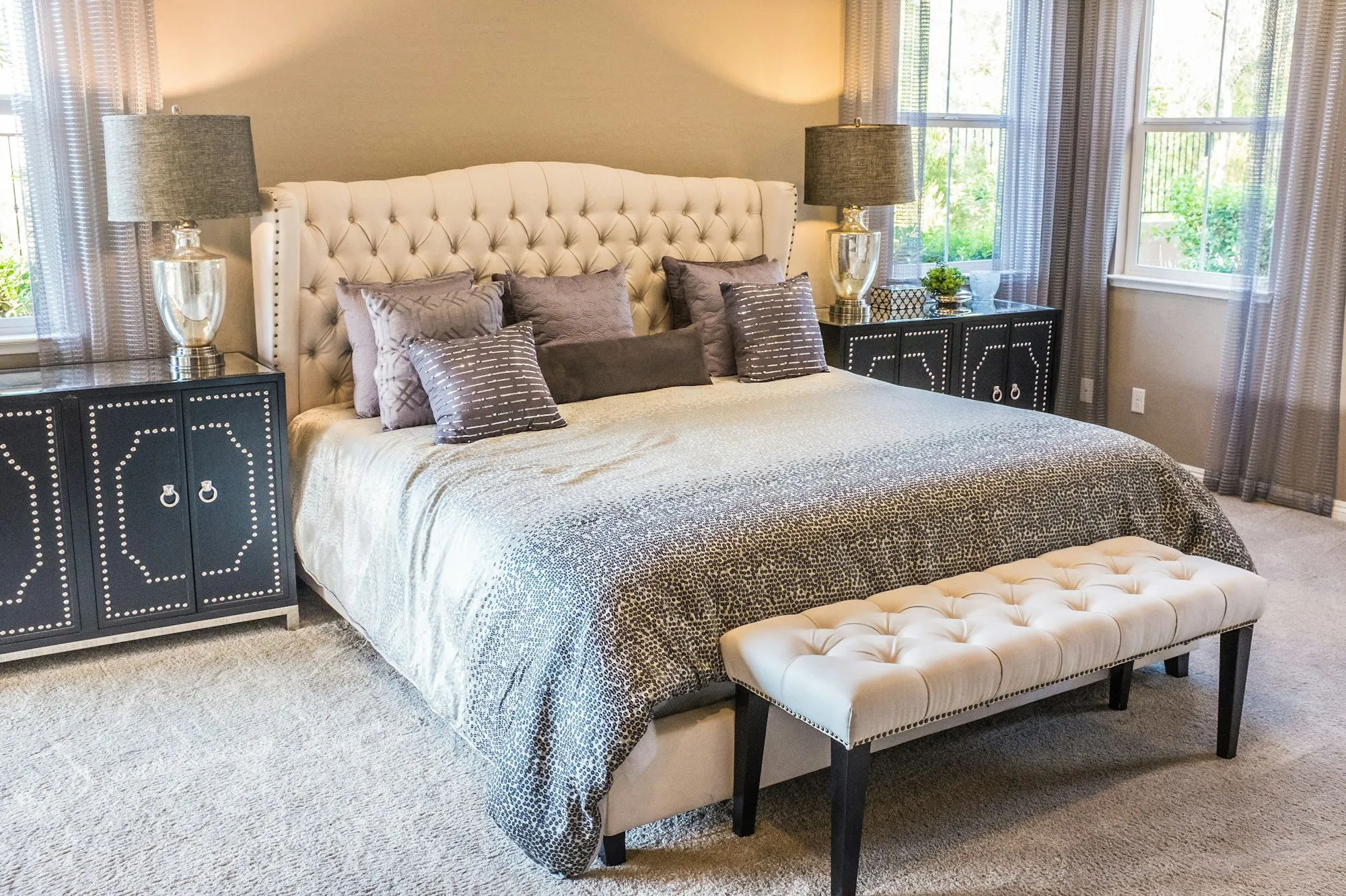 A bright bedroom with an upholstered headboard and a bench at the foot of the bed